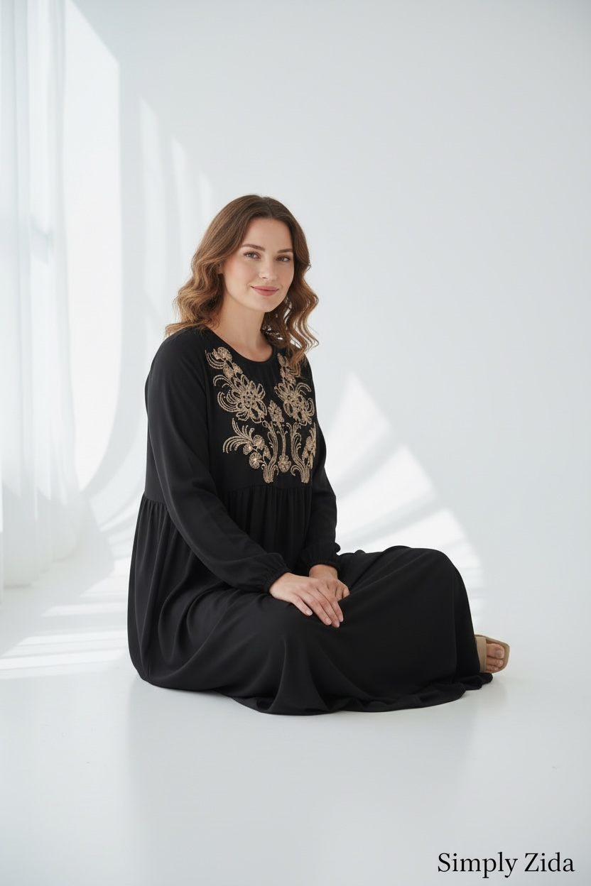 Elegant black modest abaya with intricate gold embroidery and long sleeves shown in seated pose.