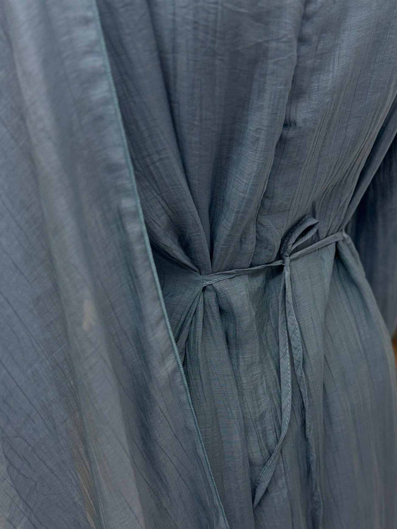 Close-up of a blue dress with a tie detail on a neutral background